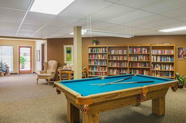 Green felt pool table in front of large book shelves filled with books in the Longmont Regent game room and library
