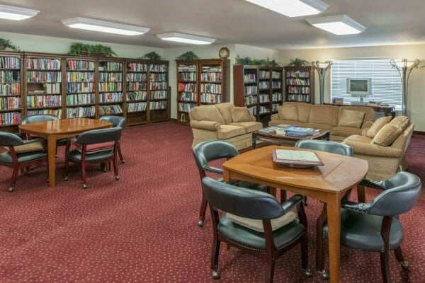 Library with four large book shelves filled with books, tables and chairs and loveseats at Shasta Estates