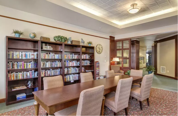 The library area at Merrill Gardens at Tacoma, with chairs at a long table in front of shelves of books