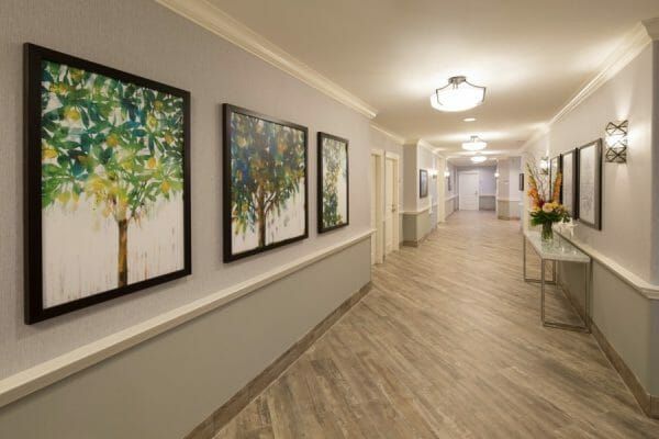 Hallway with paintings on the wall and a table with orange flowers at Oakmont of Pacific Beach