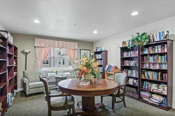 Seaton Voorhees' library, with bookshelves on the left and right walls, armchairs near a window, and a table and two chairs in the middle of the room