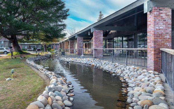 A rock-lined stream running alongside a covered patio area at The Atrium at Carmichael