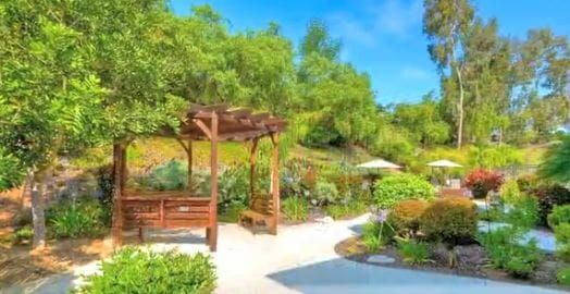 Courtyard at Hospice of North Coast. Includes a wooden gazebo around a walkway with flowers, shrubs and trees.