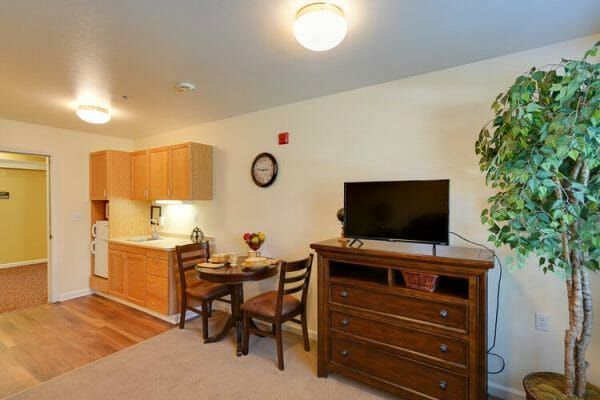 Model room includes dresser with flat screen tv, dining table with two chairs, kitchenette with refrigerator, countertop and cabinets at Orchard Park