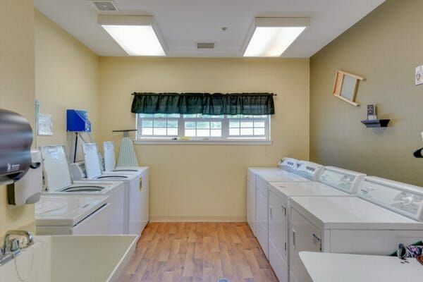 Laundry room includes four washing machines on the left side beside a large sink and four dryers on the right side beside a table at Orchard Park