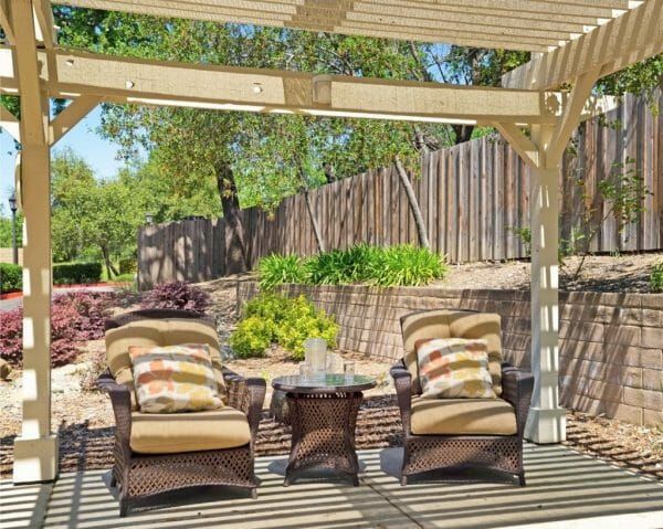 Outdoor cushioned wicker chairs under a trellis on the patio of Sunrise of Fair Oaks