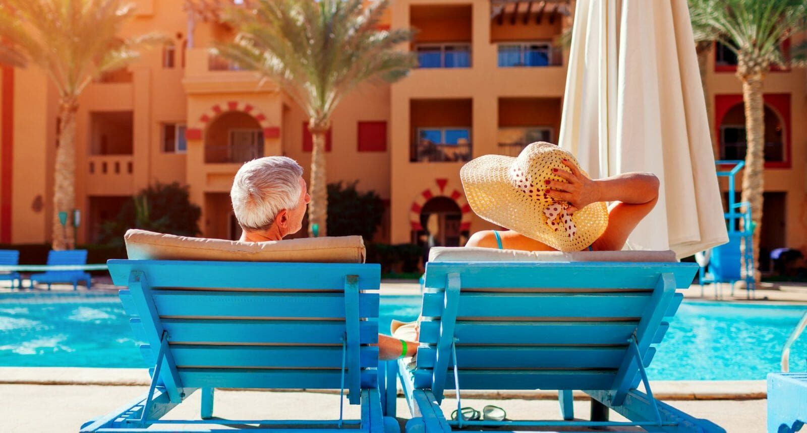 Senior couple relaxing by the pool on teal lounge chairs