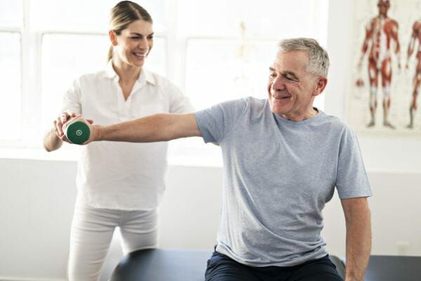 Senior man lifting weights with assistance from a female rehab specialist