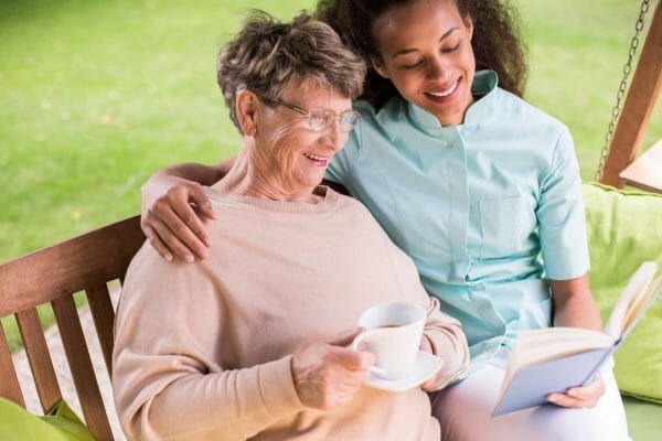 Senior woman drinking coffee seated next to a female caregiver