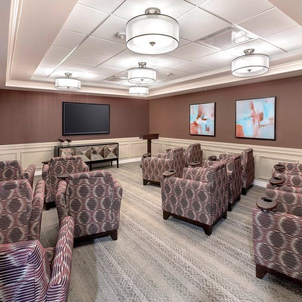 Comfortable armchairs with built-in drink holders arranged in front of a tv in the media room at Brooklyn Pointe Assisted Living & Memory Care
