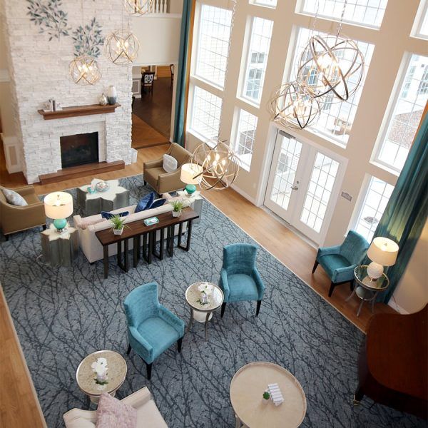A bird's-eye view of the great room at Maumee Pointe Assisted Living & Memory Care, showing multiple sitting areas, a wall of windows and a floor-to-ceiling fireplace
