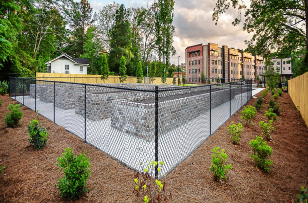 A fenced-in area with multiple large, raised garden beds, and The Ashbury apartment building in the background