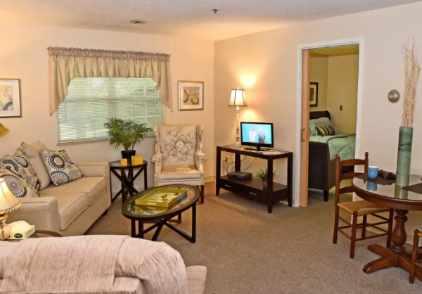 A model apartment living room at O’Neill Healthcare Bay Village, with a partial view into the bedroom