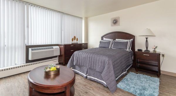 A model studio apartment at Skyline Tower Senior Apartments, furnished with a bed, dresser, nightstand, and a coffee table