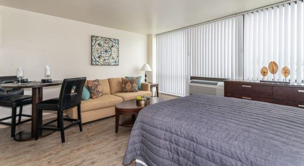 Another view of Skyline Tower Senior Apartments' model studio apartment, showing the foot of a bed, a coffee table, a couch, and a small dining table