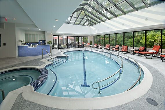 Allegro Harrington Park's indoor pool, with ramp access, a spa tub, lounge chairs, and a glassed-in, vaulted ceiling