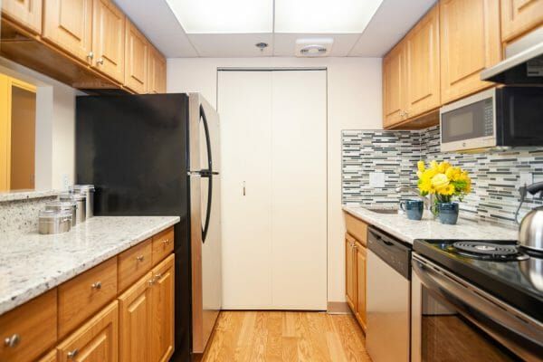 The galley kitchen of a model apartment at Five Star Premier Residences of Teaneck. with stainless steel appliances and a cut-out into the living room