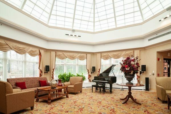 Five Star Premier Residences of Teaneck's community living room, with a grand piano and dramatic glass, peaked ceiling