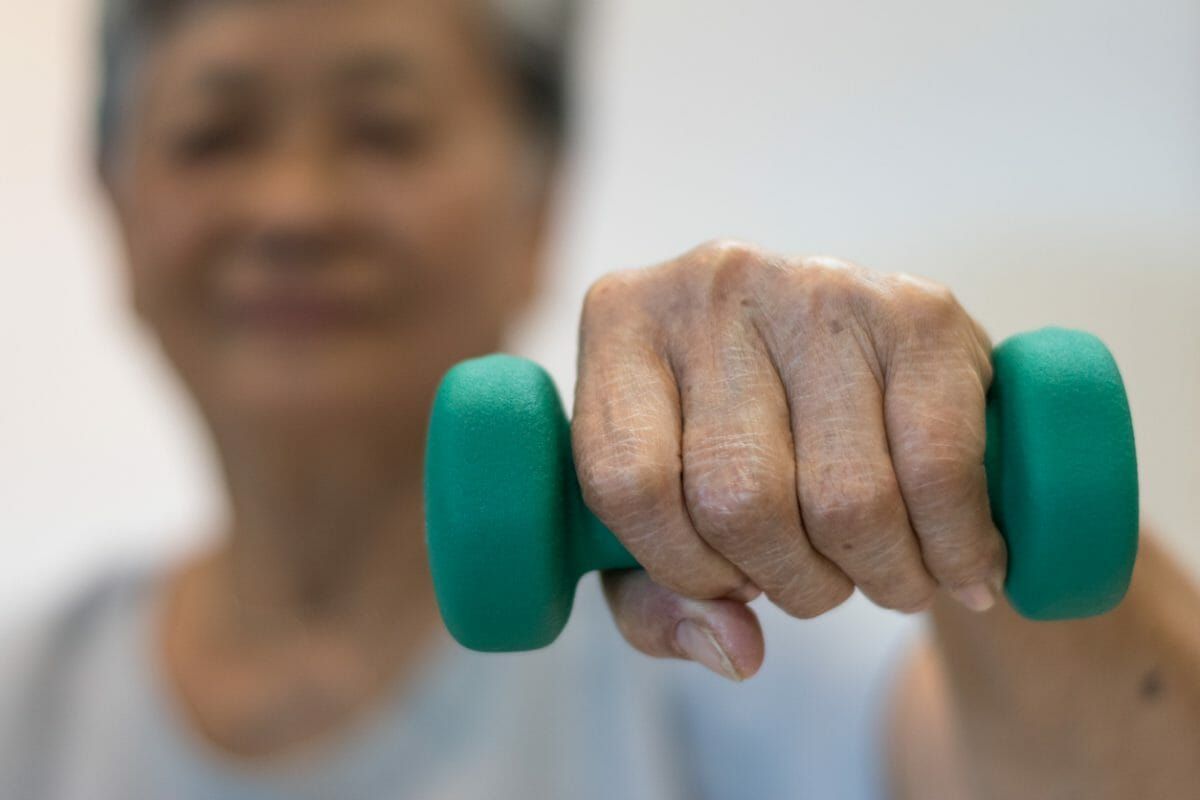 Senior elderly Asian woman hand holding dumbbell in physical therapy session.