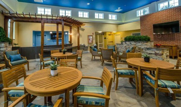 Tables and chairs and a wall-mounted tv in Artis Senior Living of Princeton Junction's common area and gathering room