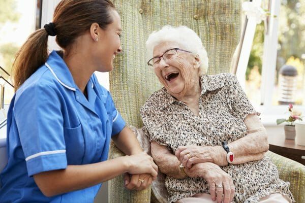 Senior-Woman-Sitting-In-Chair-And-Laughing-With-Nurse-In-Retirement-Home-1047536650_2125x1416-scaled.jpeg