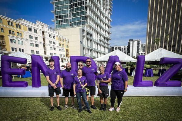 Group of people in purple shirts posing in front of an inflatable END ALZ display on a grass surface on a sunny day
